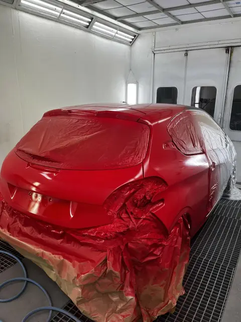 Voiture rouge fraîchement repeinte dans la cabine de peinture de l'atelier